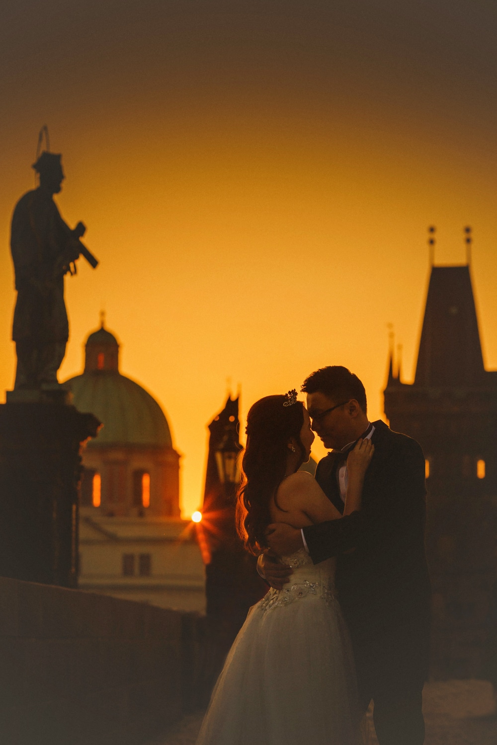 Prague, Charles Bridge sunrise, couple embracing, wedding dress, yellow sky, sun flare, statues